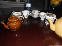 Overall view of two teapots, teacups with saucers and loose teacups on a dark wooden table.