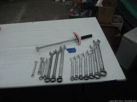Photo shows a collection of 13 used combination wrenches arranged on a table beside a long torque wrench with a black handle, with a blue tag labeled 'Lot 21'