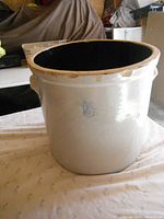 Full view of the oval cream-colored stoneware crock with two side handles. Shows significant chipping and wear along the upper rim.