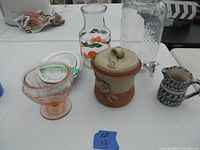 View of all items in the lot including juice jar, punch dispenser, pottery jar, pink depression glass, pottery pitcher, ironstone plates
