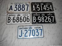Six vintage Ontario single license plates from 1951, 1959, 1962, 1963, and two from 1966 shown on a table.