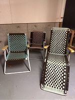 Photo showing the three folding lawn chairs placed on a concrete floor in a basement area. Includes two upright chairs with woven macrame seats and backs in two different color combinations, and one lounger reclined with matching woven macrame.