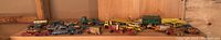 Full view of all vintage metal toy cars and trucks lined up on wooden shelf.