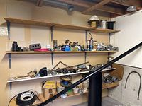 Wide view of four shelves containing assorted electrical and plumbing supplies including wires, connectors, pipes, tape, and fittings.