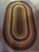 Large oval braided area rug with alternating bands of brown and tan shades shown against a light floor