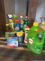 Photo showing multiple cleaning supplies including Lysol, OxiClean, Windex, Palmolive, Vim, Pine-Sol, Mr. Magic, Cascade detergent, and a small yellow lid container.