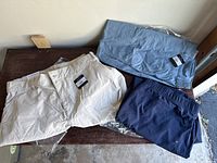 Three pairs of Eddie Bauer ankle pants in pumice, chamblue, and navy blue colors shown folded on a table, with tags attached to indicate new condition.