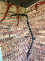 Photo showing black metal scythe mounted on brick wall with red metal horse hitches above