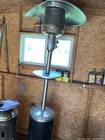 Full assembled propane patio heater with reflective top in a wooden shed.