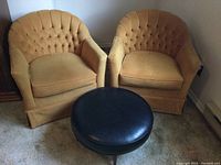 Two mustard velvet tub chairs with black round ottoman on carpet