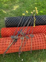Nine metal re-bar fence posts with yellow plastic caps and metal stabilizing plates placed on top of the snow fence rolls.