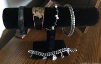 Photo of five bracelets displayed on black velvet bracelet stand, four on the stand, one below it showing charm bracelet details.
