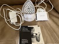 Photo of Tanda Professional light therapy device showing main unit with multiple LED treatment heads, power cable, and replacement treatment head along with user manual booklet.