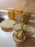 Photo of vintage Tupperware plastic kitchen containers including tall Pick-A-Dillys, small containers with lids, divided serving dish and scoops on kitchen counter.