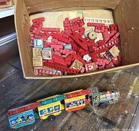 Photo showing Disneyland metal windup train with multiple cars featuring Mickey and Donald Duck images next to a box of red plastic interlocking building blocks and wooden alphabet blocks.