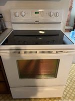 Full front view of white Whirlpool electric oven/stove combination showing glass cooktop, control knobs, and oven window.