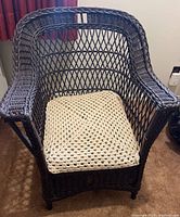 Front view of dark brown wicker armchair with beige crocheted cushion on seat.