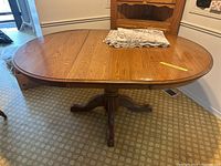 Full view of the oval wooden pedestal table showing wood grain and folded lace tablecloth on top.