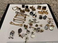 Overview of all cufflinks, tie bars, tie tacks and shirt studs arranged on white background