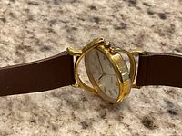 Side view showing gold-tone hinged bezel flipped open and brown leather strap.