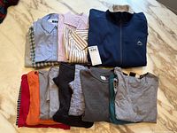 Folded assorted men's shirts and T-shirts, various colors and styles, on marble table