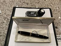 Open Montblanc presentation box showing black fountain pen in slot and separate ink bottle with cap on lid