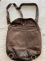 Top view of the brown leather knapsack with visible wear and adjustable strap laid flat.