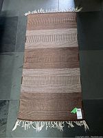 Full view of rectangular brown and cream striped wool rug with fringed edges laid on tiled floor.