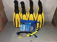 Photo of four yellow and black Mares snorkeling fins, two snorkels (yellow and blue), and PADI literature in a blue zippered pouch.