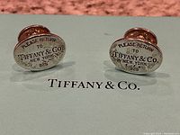 Two oval sterling silver cufflinks engraved "Please Return to Tiffany & Co. New York 925" displayed on Tiffany & Co blue box