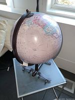 Photo of entire vintage style globe on airplane-shaped cast metal base, showing side view and globe tilt.