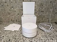 Google Nest Wifi router with open box, showing the device, a white power cable, and setup guide laid out on a countertop.