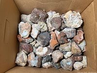 Overhead view of a box filled with numerous rock and mineral specimens, showing a mix of colors and textures.