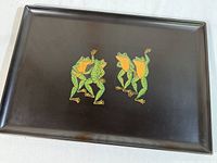 Top view of black rectangular serving tray displaying four green frogs in two pairs dancing, centered on tray surface