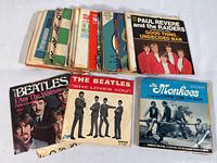 Photo of a stack of approximately 45 vintage vinyl records with visible titles including Paul Revere and the Raiders and many others