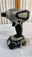 Front and side views of the black and white Makita cordless drill showing model labeling, worn body, textured grip, and battery attached at the base.