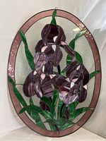 Full front view of the oval stained glass panel showing purple flowers, green leaves, textured clear background and pink border.