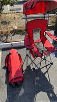 One red Renetto folding backpack chair opened with sun/weather hood, mesh seat and back, cup holder on armrest, and one chair folded beside it