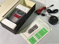 Opened box revealing the portable CB radio handheld unit packed in styrofoam blocks, wrapped in plastic, with owner's manual and wiring accessories including a power cable and antenna.