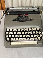 Front view of gray Smith Corona Sterling portable typewriter showing full keyboard and paper holder.