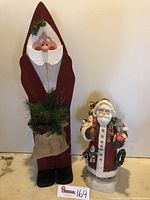 Full view of two Santa figurines: tall handcrafted wooden Santa with burlap sack and smaller musical Santa.