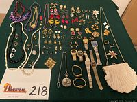 Overall view of all items displayed on green cloth: necklaces, earrings, brooch, watches, pocket watch, bag