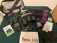 Wide overhead shot showing camera with attached lens, additional lenses, battery charger, remote, cases, manuals and camera bag on table