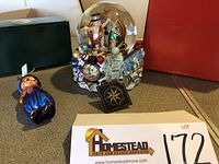 Photo showing Radko Millennium Extravaganza Glitterglobe music box with original box behind and Radko sailor boy glass ornament in blue outfit with original green box.