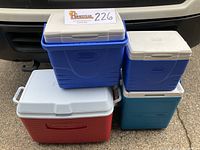Four coolers in a group including red Rubbermaid, blue Coleman (two sizes), and teal Rubbermaid coolers