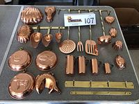 Full collection of copper molds and utensils arranged on table showing various shapes and sizes with brass hanging bars