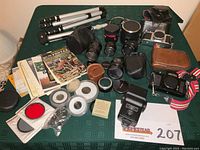 Wide view of entire lot arranged on green tablecloth showing cameras, lenses, cases, tripod, filters, and manuals.