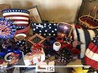 Tabletop display showing large bowls, mugs, pillows, baskets, decorative trays, candleholders, and small flags all in red, white, and blue patriotic theme.