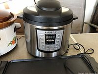 Front view of Instant Pot IP-LUX with digital control panel visible alongside other appliances on counter.