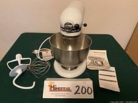 Front view of KitchenAid stand mixer with attachments and instruction booklet on green surface.